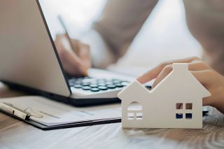 Foto: Person am Laptop mit Häuschen davor